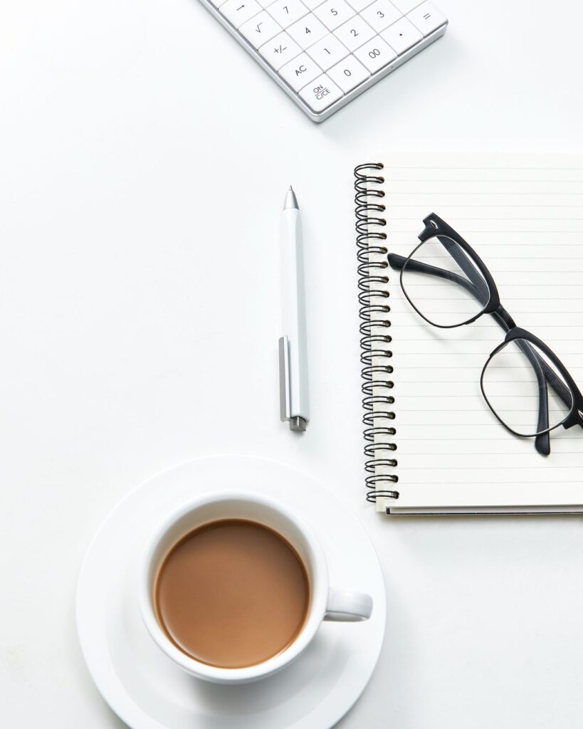 Schreibtisch von oben mit Notizbuch, Brille und Kaffeetasse